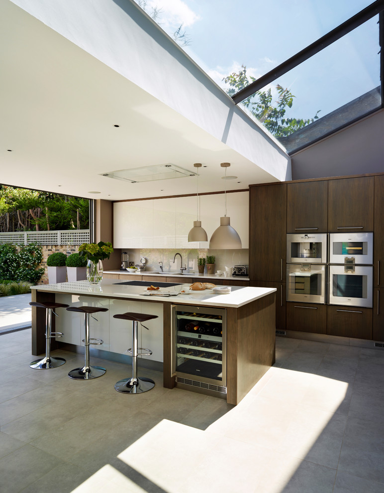 Example of a large trendy open concept kitchen design in London with an island, flat-panel cabinets, quartzite countertops, white backsplash, glass tile backsplash and stainless steel appliances