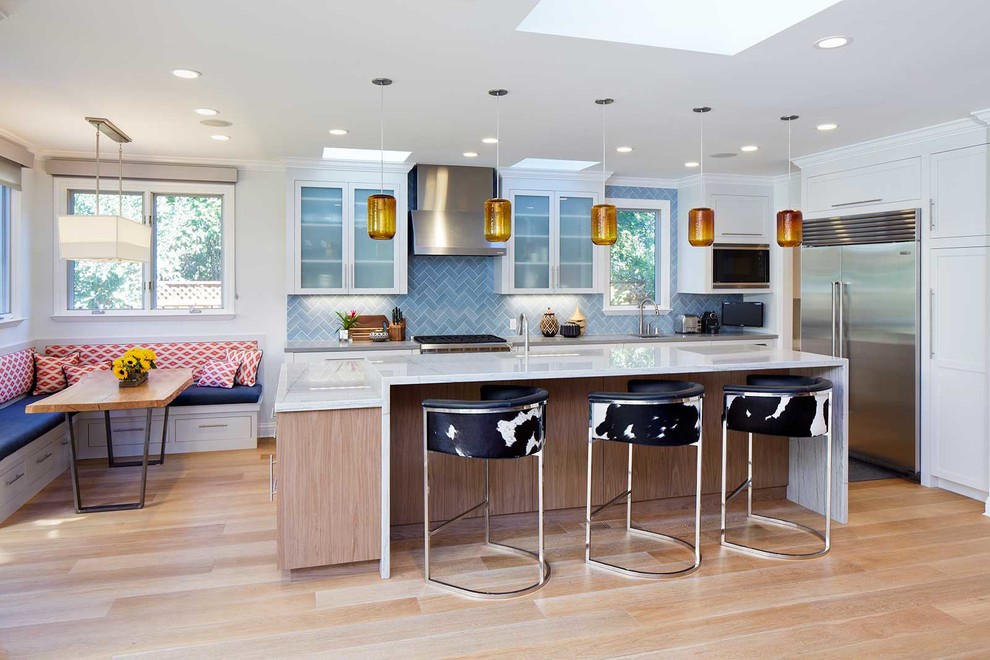 Traditional l-shaped open plan kitchen in San Francisco with a submerged sink, glass-front cabinets, white cabinets, marble worktops, blue splashback, porcelain splashback, stainless steel appliances, light hardwood flooring and an island.