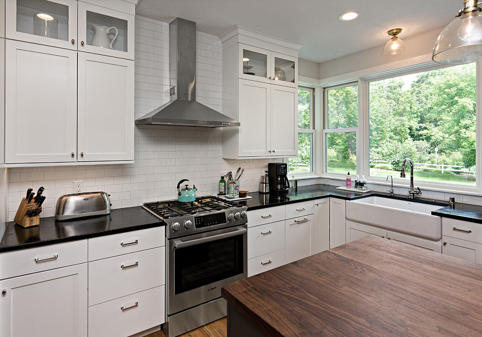 Foto på ett mellanstort lantligt svart u-kök, med vitt stänkskydd, stänkskydd i keramik, rostfria vitvaror, mellanmörkt trägolv, en köksö, brunt golv och släta luckor