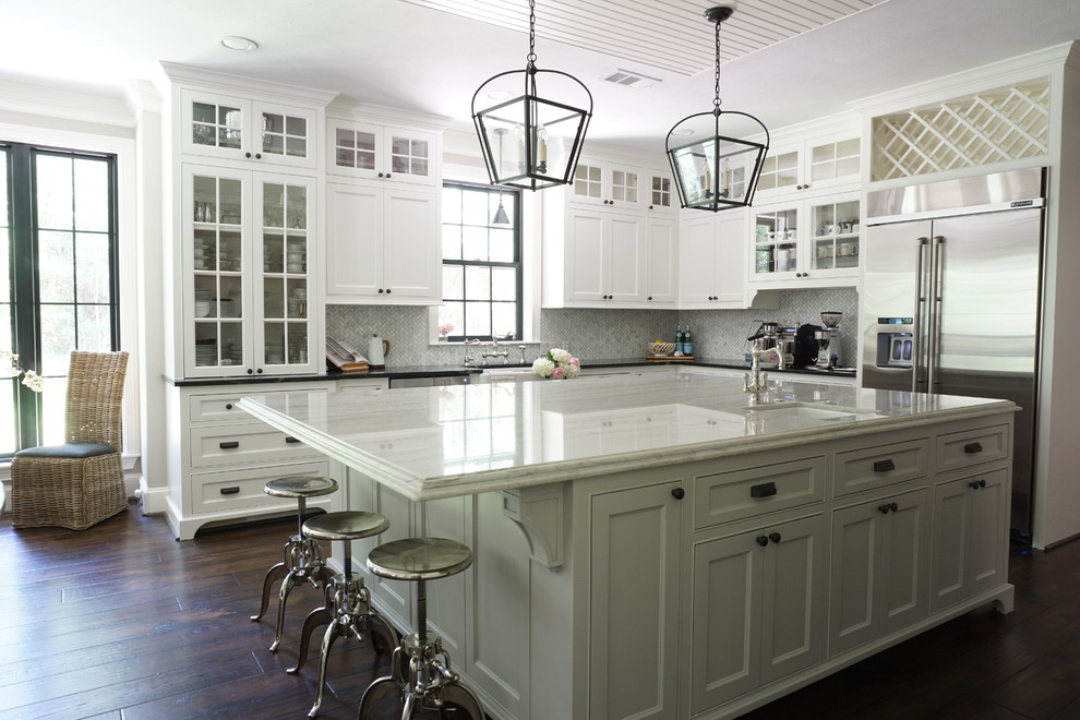 Lantlig inredning av ett vit vitt l-kök, med en rustik diskho, luckor med infälld panel, vita skåp, rostfria vitvaror, mörkt trägolv, en köksö och brunt golv