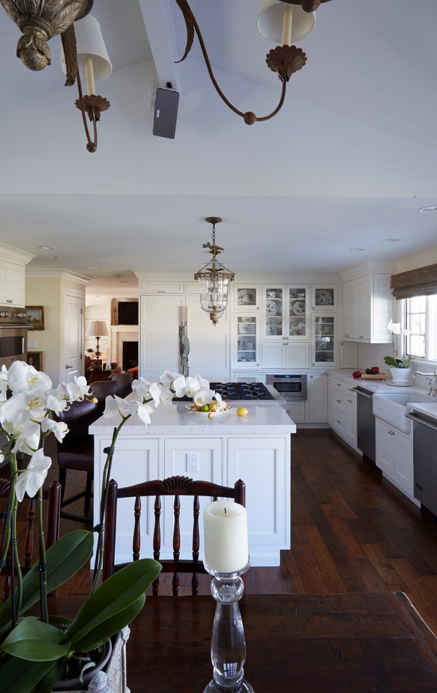 Lantlig inredning av ett stort vit vitt kök, med en rustik diskho, skåp i shakerstil, vita skåp, mörkt trägolv, en köksö, bänkskiva i kvartsit, vitt stänkskydd, stänkskydd i keramik, integrerade vitvaror och brunt golv