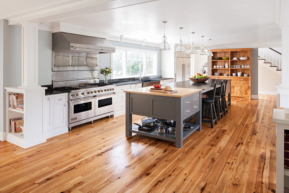 Kitchen - large contemporary medium tone wood floor kitchen idea in Boston with a farmhouse sink, recessed-panel cabinets, white cabinets, soapstone countertops, black backsplash, stone slab backsplash, stainless steel appliances and an island
