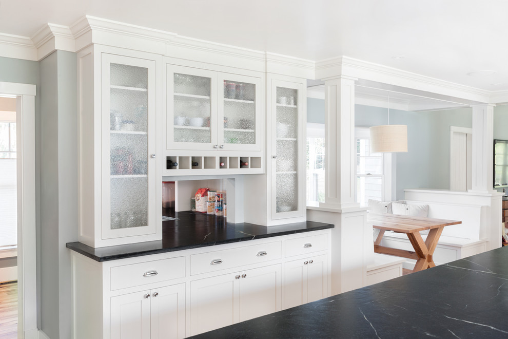 Kitchen pantry - large contemporary medium tone wood floor kitchen pantry idea in Boston with a farmhouse sink, recessed-panel cabinets, white cabinets, soapstone countertops, black backsplash, stone slab backsplash, stainless steel appliances and an island