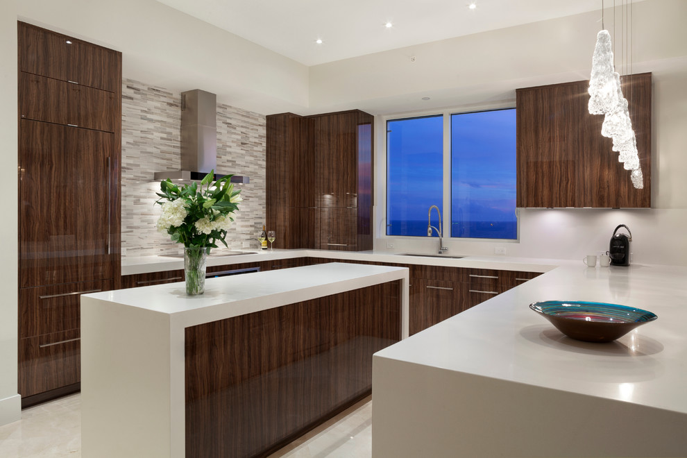 Moderne Küche mit flächenbündigen Schrankfronten, hellbraunen Holzschränken, Quarzwerkstein-Arbeitsplatte, Küchenrückwand in Grau, Elektrogeräten mit Frontblende und Kücheninsel in Miami