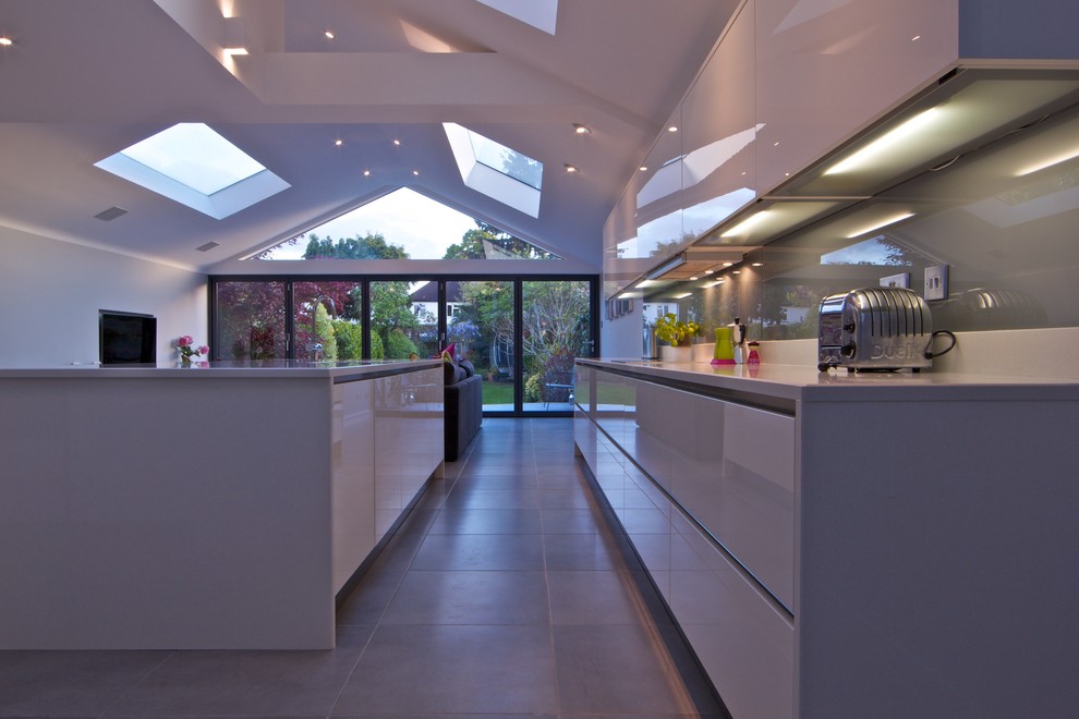 Large trendy ceramic tile kitchen photo in London with flat-panel cabinets, white cabinets, granite countertops, gray backsplash, glass tile backsplash and an island