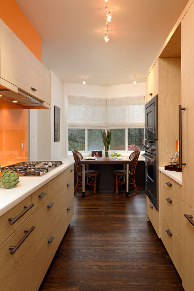 Inspiration pour une cuisine parallèle design en bois brun de taille moyenne avec un placard à porte plane, une crédence orange, une crédence en feuille de verre, un électroménager noir, un sol en bois brun, aucun îlot, un sol marron et un plan de travail blanc.