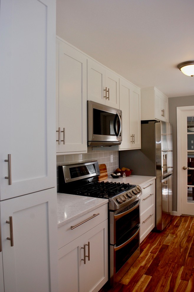 Inspiration for a mid-sized transitional galley medium tone wood floor open concept kitchen remodel in Portland with an undermount sink, shaker cabinets, white cabinets, quartz countertops, gray backsplash, ceramic backsplash, stainless steel appliances, no island and gray countertops