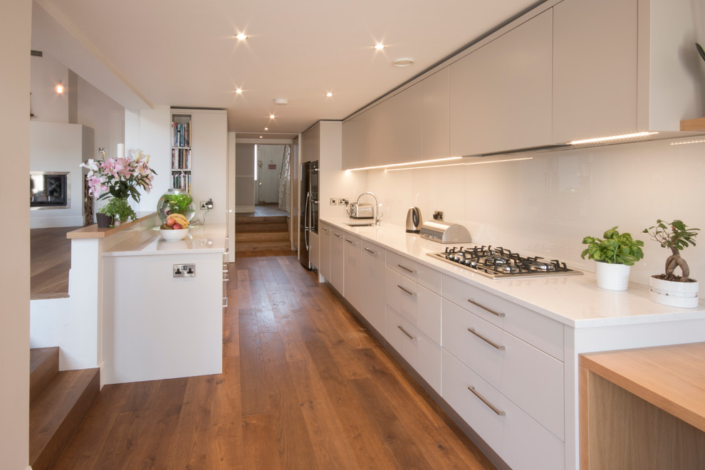 Inspiration for a medium sized contemporary galley enclosed kitchen in Other with a built-in sink, flat-panel cabinets, beige cabinets, engineered stone countertops, white splashback, glass sheet splashback, stainless steel appliances and medium hardwood flooring.
