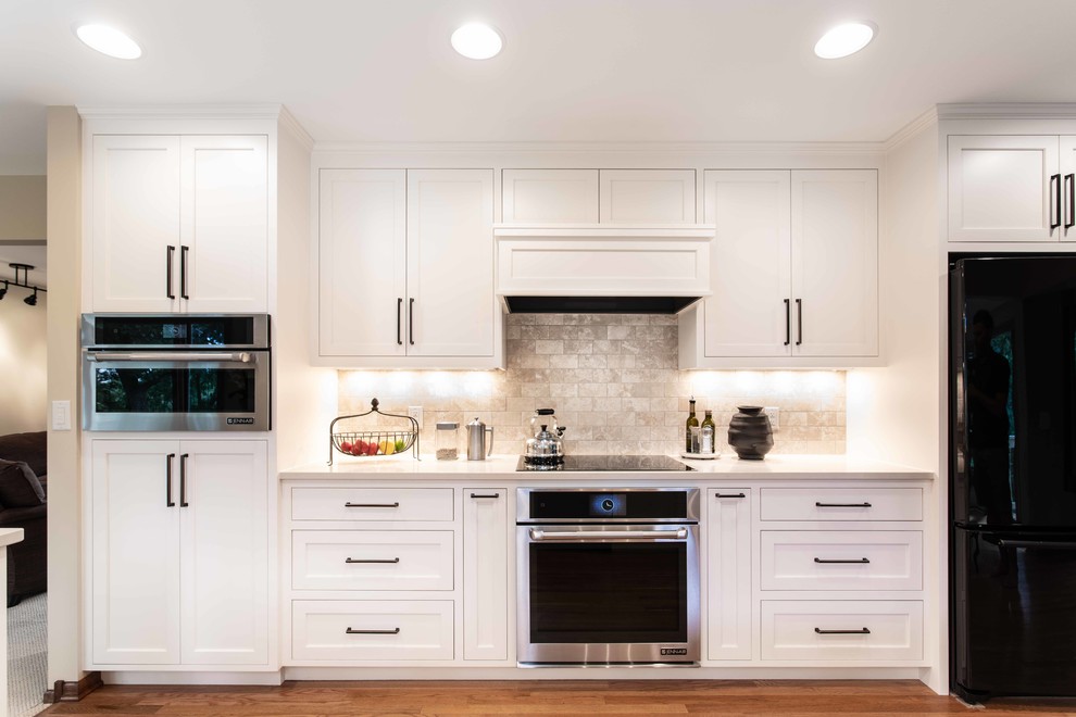 This is an example of a large contemporary galley kitchen/diner in Minneapolis with a submerged sink, recessed-panel cabinets, white cabinets, engineered stone countertops, white splashback, stainless steel appliances, medium hardwood flooring, a breakfast bar and white worktops.