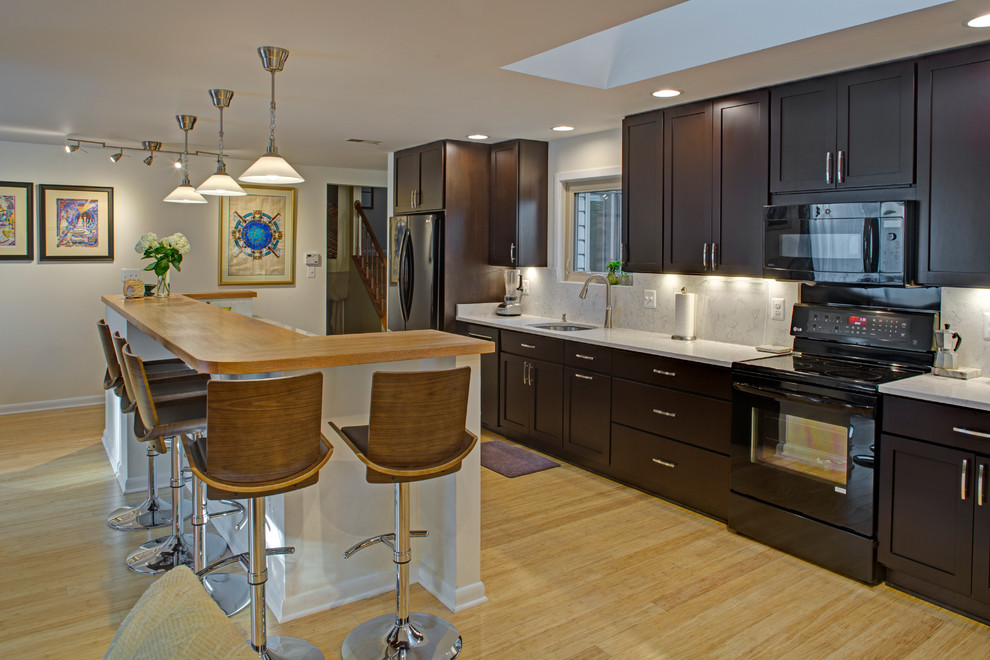 Example of a small trendy galley bamboo floor kitchen design in Baltimore with an undermount sink, shaker cabinets, dark wood cabinets, quartz countertops, stone tile backsplash, black appliances and an island
