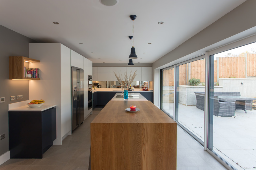 Photo of an expansive contemporary l-shaped kitchen/diner in Hertfordshire with a built-in sink, flat-panel cabinets, blue cabinets, quartz worktops, metallic splashback, mirror splashback, stainless steel appliances, porcelain flooring, an island, white floors and white worktops.