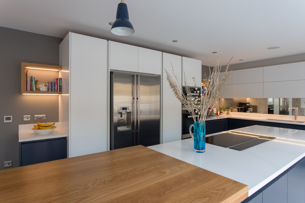 Expansive contemporary l-shaped kitchen/diner in Hertfordshire with a built-in sink, flat-panel cabinets, blue cabinets, quartz worktops, metallic splashback, mirror splashback, stainless steel appliances, porcelain flooring, an island, white floors and white worktops.