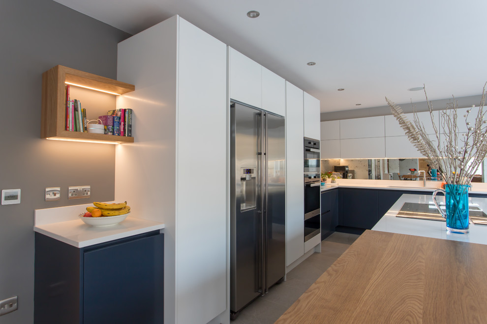 Design ideas for an expansive contemporary l-shaped kitchen/diner in Hertfordshire with a built-in sink, flat-panel cabinets, blue cabinets, quartz worktops, metallic splashback, mirror splashback, stainless steel appliances, porcelain flooring, an island, white floors and white worktops.