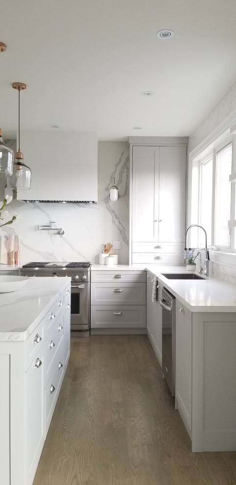 Large trendy u-shaped light wood floor and gray floor eat-in kitchen photo in Toronto with a single-bowl sink, shaker cabinets, gray cabinets, quartz countertops, white backsplash, stone slab backsplash, stainless steel appliances and an island