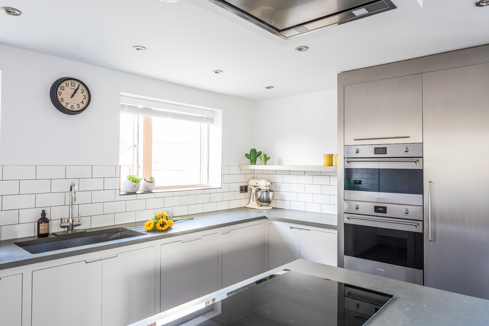 Large contemporary u-shaped open plan kitchen in Other with a submerged sink, flat-panel cabinets, grey cabinets, engineered stone countertops, white splashback, metro tiled splashback, stainless steel appliances, ceramic flooring, an island and grey floors.