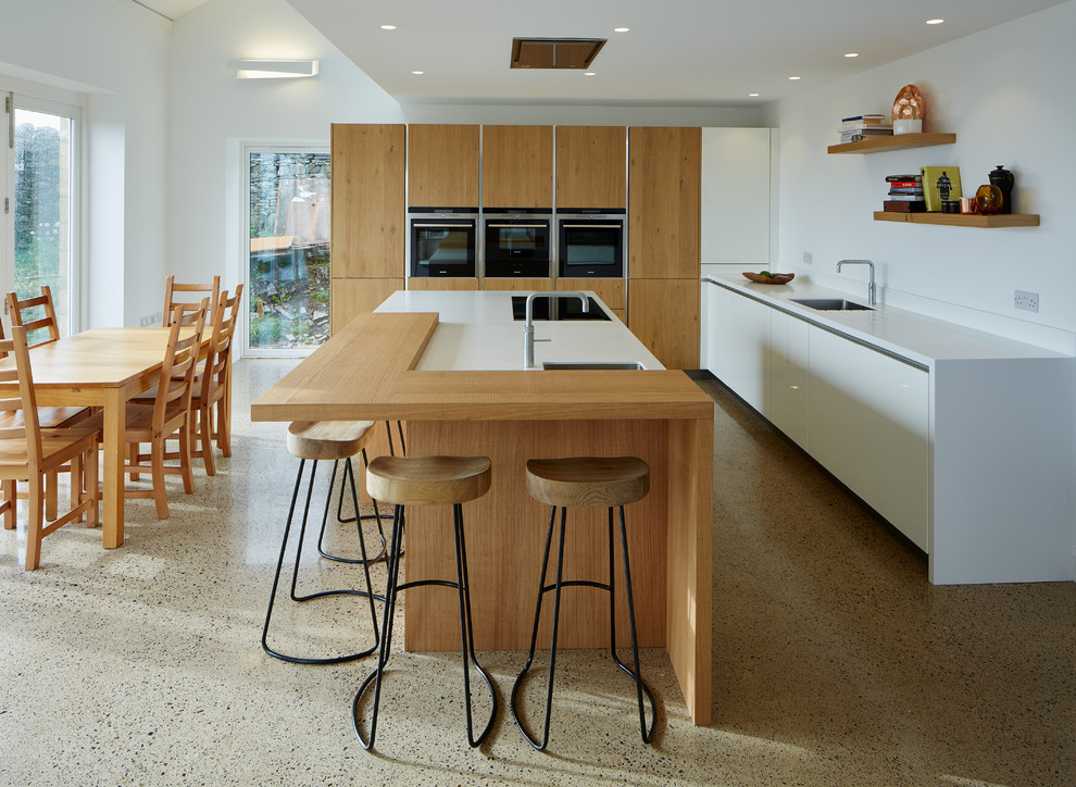 Cette photo montre une grande cuisine ouverte tendance en L et bois brun avec un plan de travail en surface solide, un électroménager noir, sol en béton ciré, îlot et un sol beige.