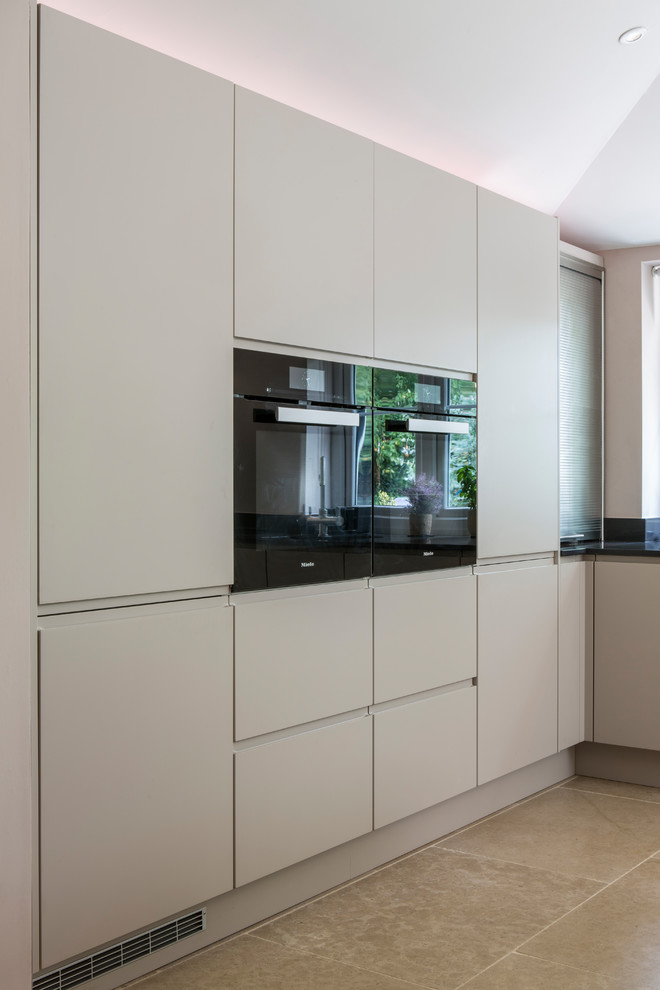 Photo of a large contemporary u-shaped open plan kitchen in Oxfordshire with an integrated sink, flat-panel cabinets, grey cabinets, quartz worktops, black appliances, travertine flooring, a breakfast bar and black worktops.