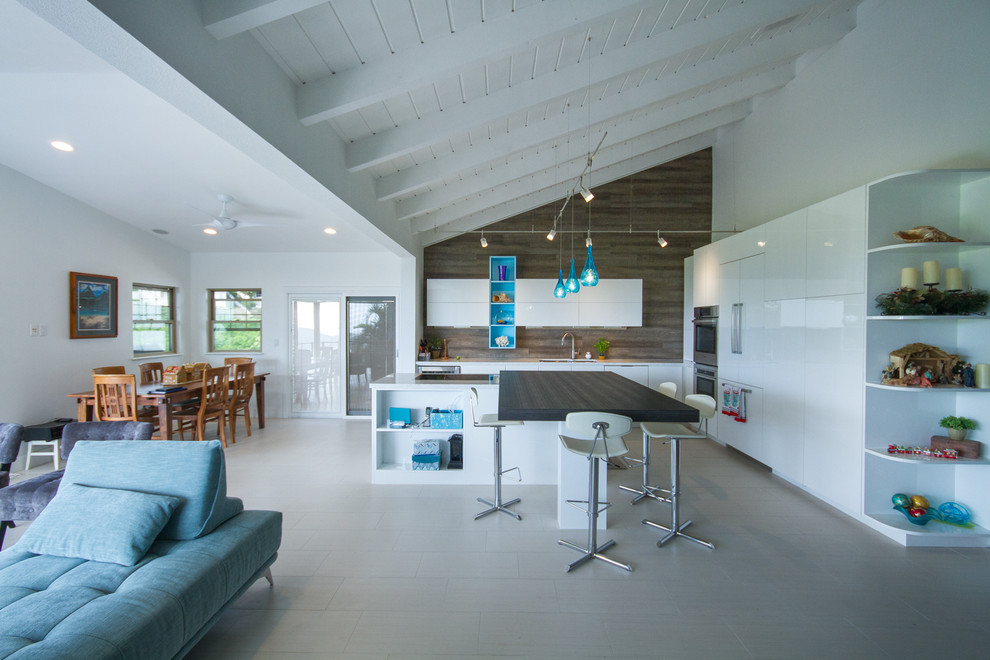 This is an example of a large contemporary l-shaped kitchen/diner in Hawaii with a submerged sink, flat-panel cabinets, white cabinets, wood worktops, brown splashback, integrated appliances, ceramic flooring and an island.