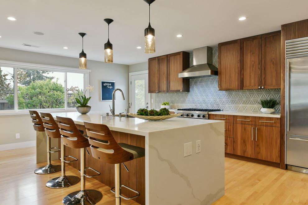 Immagine di una cucina design con lavello sottopiano, ante lisce, ante in legno bruno, paraspruzzi grigio, elettrodomestici in acciaio inossidabile, parquet chiaro e top beige