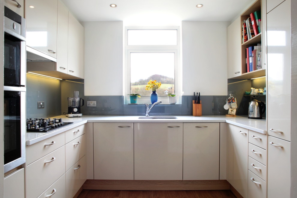 Inspiration for a small contemporary u-shaped enclosed kitchen in Buckinghamshire with blue splashback, glass sheet splashback, stainless steel appliances, no island, flat-panel cabinets, beige cabinets, quartz worktops, medium hardwood flooring and an integrated sink.