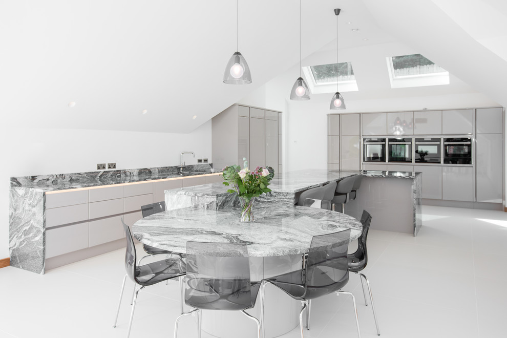 Contemporary kitchen in Cornwall with a submerged sink, flat-panel cabinets, grey cabinets, marble worktops, grey splashback, marble splashback, black appliances, an island, white floors and grey worktops.