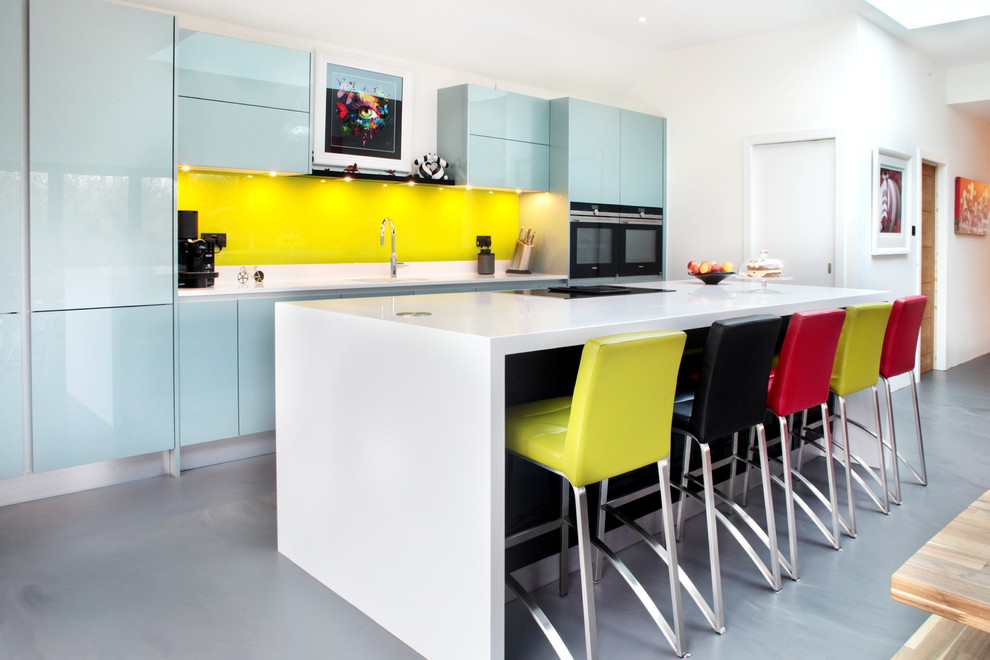 Zweizeilige, Mittelgroße Moderne Küche mit flächenbündigen Schrankfronten, blauen Schränken, Küchenrückwand in Gelb, Glasrückwand, schwarzen Elektrogeräten, Kücheninsel, grauem Boden und weißer Arbeitsplatte in Buckinghamshire