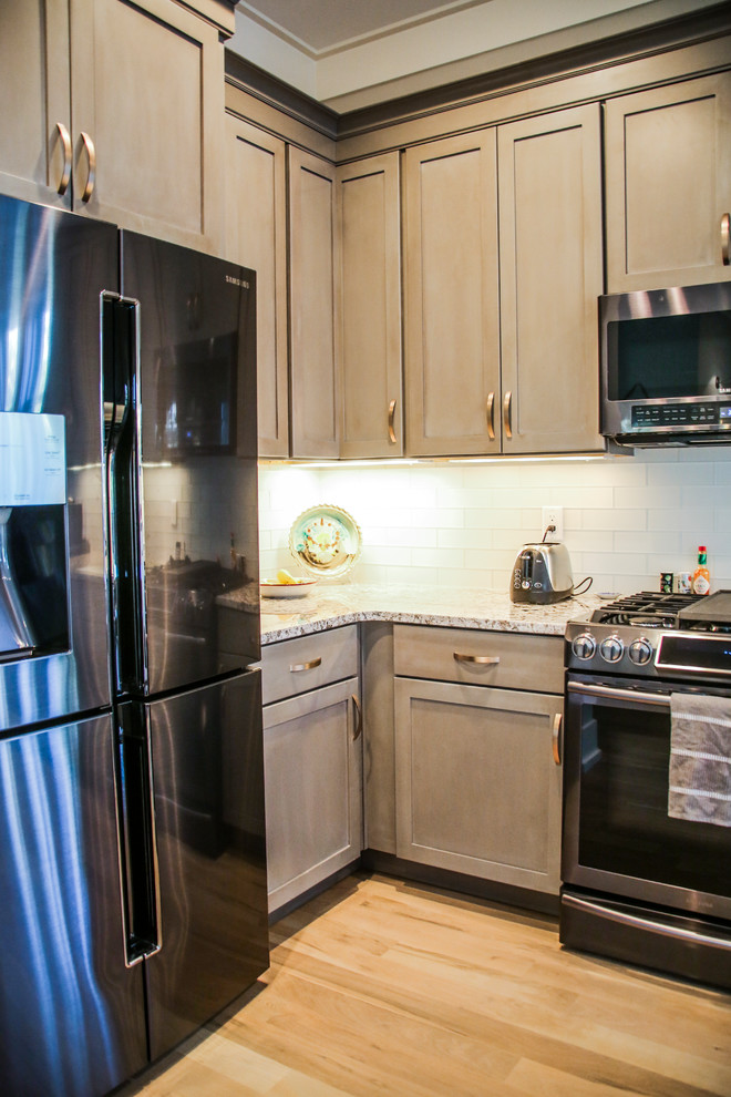 Foto på ett stort funkis flerfärgad kök, med en nedsänkt diskho, luckor med infälld panel, grå skåp, granitbänkskiva, vitt stänkskydd, stänkskydd i tegel, svarta vitvaror, plywoodgolv, en köksö och brunt golv