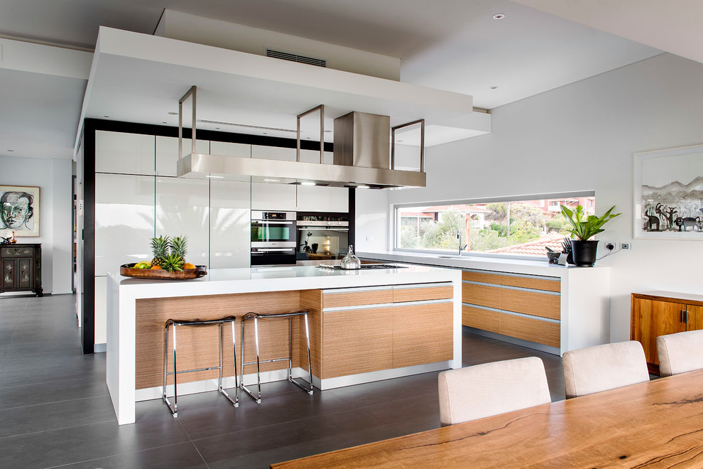 Exempel på ett modernt kök, med en undermonterad diskho, släta luckor, vita skåp, rostfria vitvaror och en köksö