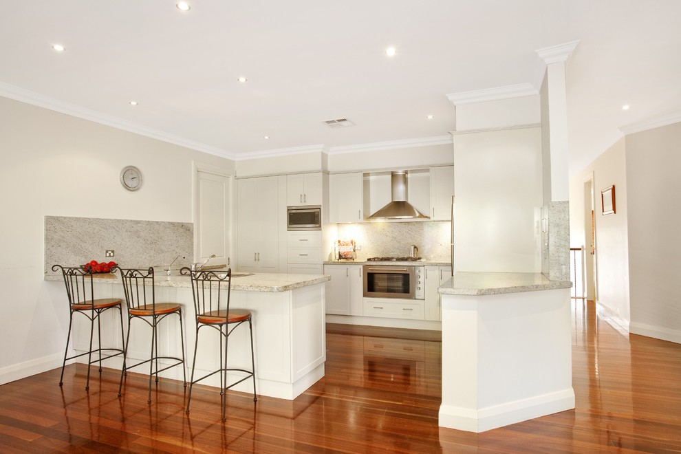 Design ideas for a medium sized contemporary galley open plan kitchen in Sunshine Coast with shaker cabinets, white cabinets, marble splashback, marble worktops, white splashback, stainless steel appliances, bamboo flooring, an island, brown floors and white worktops.