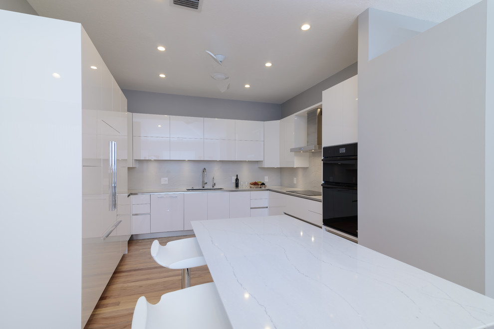 Inspiration for a mid-sized contemporary galley light wood floor enclosed kitchen remodel in Miami with a single-bowl sink, flat-panel cabinets, white cabinets, quartz countertops, white backsplash, paneled appliances and an island