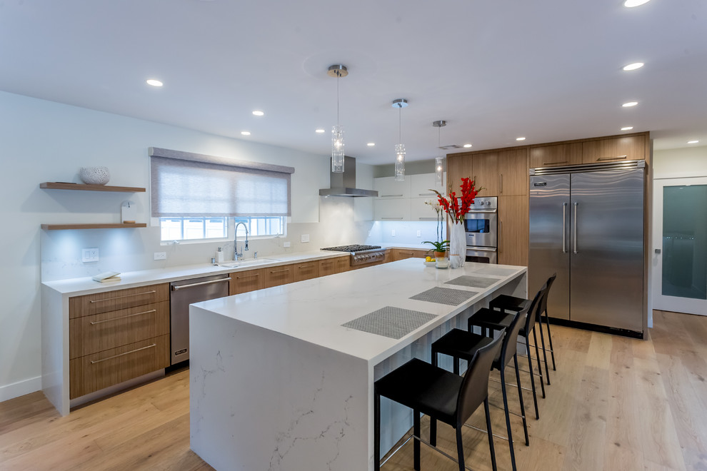 Modern inredning av ett stort kök, med en undermonterad diskho, släta luckor, skåp i mellenmörkt trä, marmorbänkskiva, rostfria vitvaror, ljust trägolv, en köksö och beiget golv