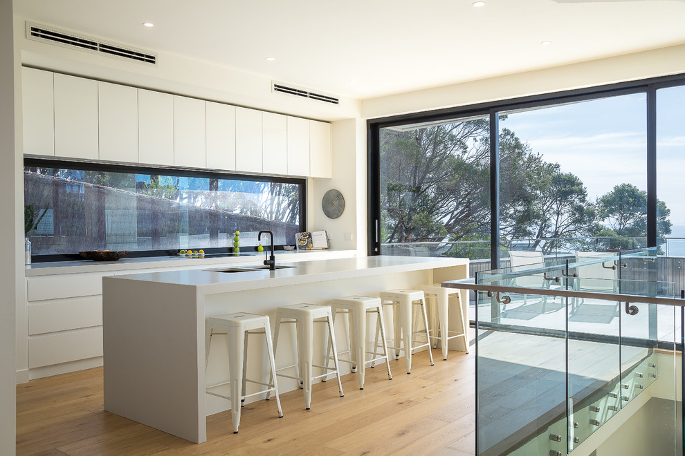 Foto de cocina actual con fregadero bajoencimera, puertas de armario blancas, una isla, salpicadero de vidrio, suelo de madera en tonos medios, suelo marrón y armarios con paneles empotrados