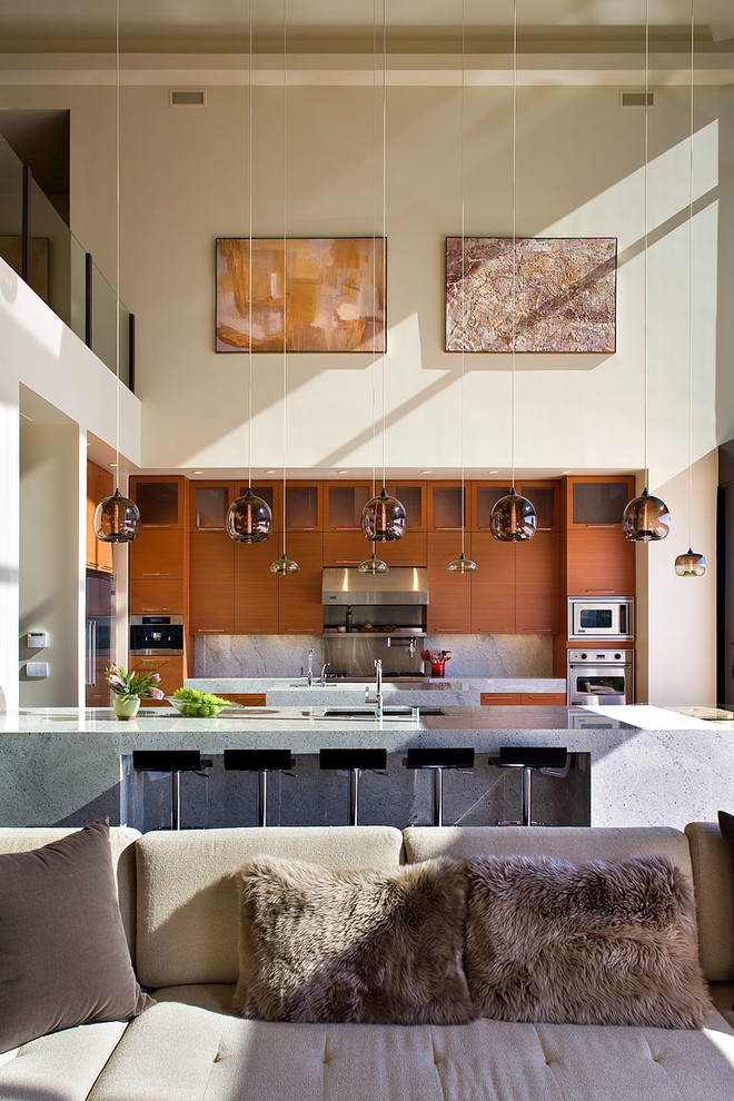 Modern inredning av ett kök, med släta luckor, skåp i mellenmörkt trä, grått stänkskydd, stänkskydd i sten och rostfria vitvaror
