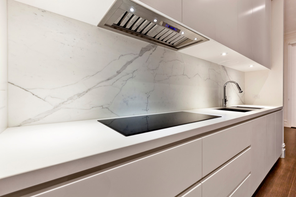 Foto på ett funkis linjärt kök och matrum, med en undermonterad diskho, släta luckor, vita skåp, marmorbänkskiva, vitt stänkskydd, stänkskydd i sten, rostfria vitvaror, mörkt trägolv och en köksö
