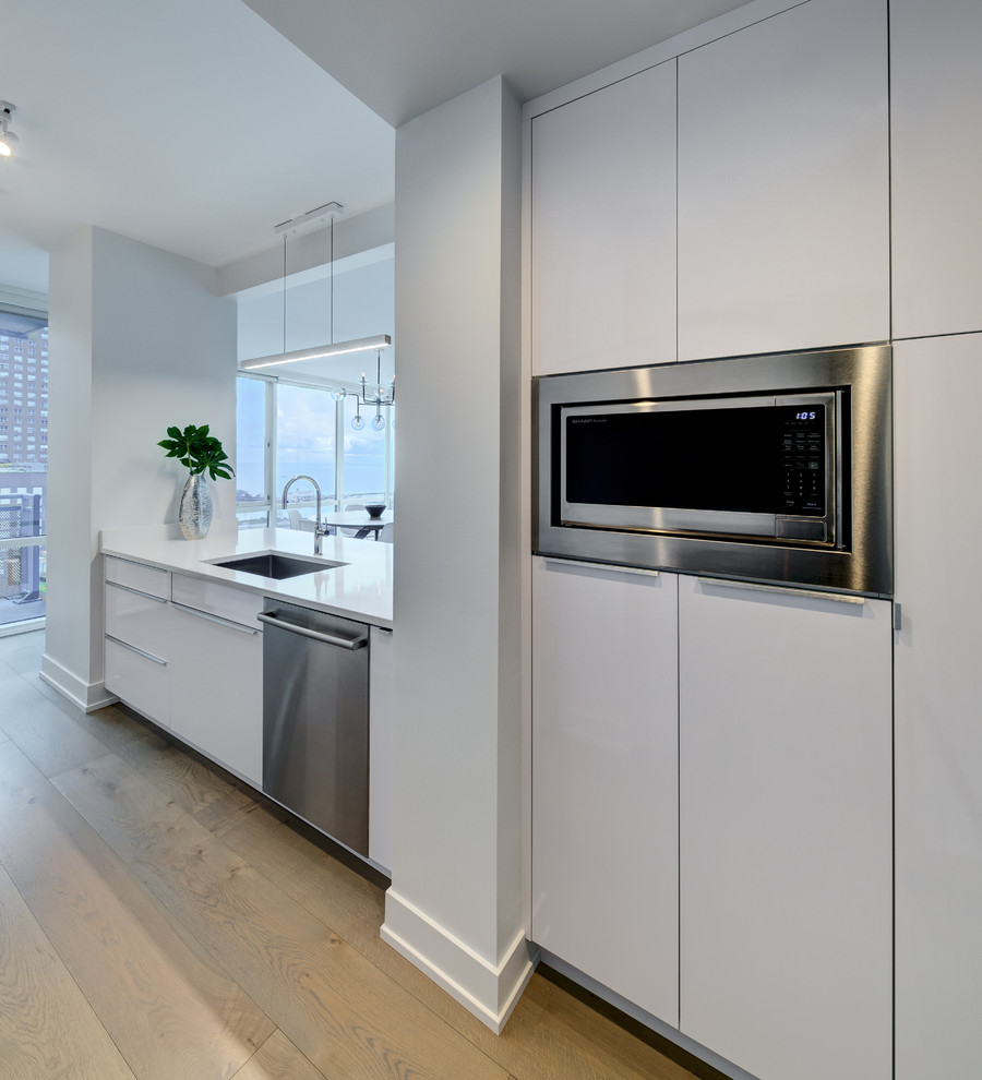 Inspiration for a small modern galley medium tone wood floor and brown floor open concept kitchen remodel in Chicago with a single-bowl sink, flat-panel cabinets, white cabinets, quartzite countertops, multicolored backsplash, stainless steel appliances, no island and white countertops
