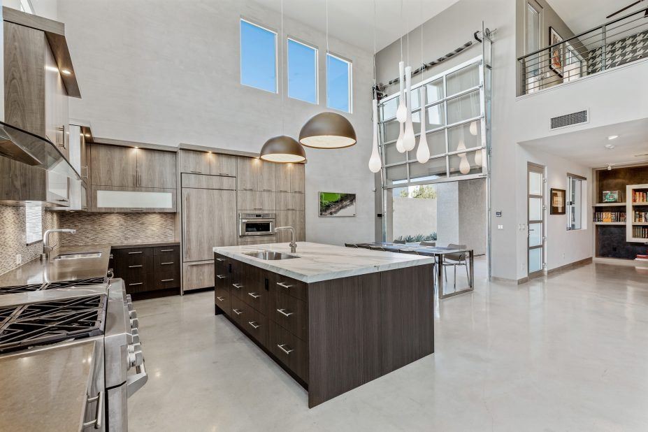 Example of a huge trendy single-wall concrete floor and gray floor open concept kitchen design in Las Vegas with an undermount sink, flat-panel cabinets, medium tone wood cabinets, granite countertops, multicolored backsplash, mosaic tile backsplash, stainless steel appliances and an island