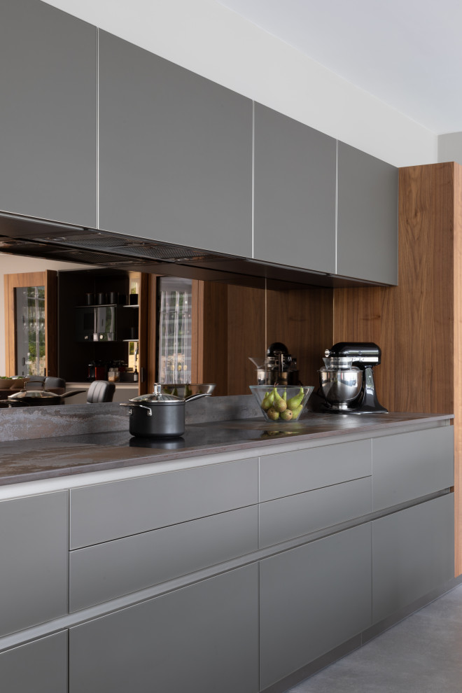 Idéer för att renovera ett stort funkis grå grått kök med öppen planlösning, med en integrerad diskho, luckor med glaspanel, grå skåp, bänkskiva i kvartsit, stänkskydd med metallisk yta, spegel som stänkskydd, svarta vitvaror och en köksö