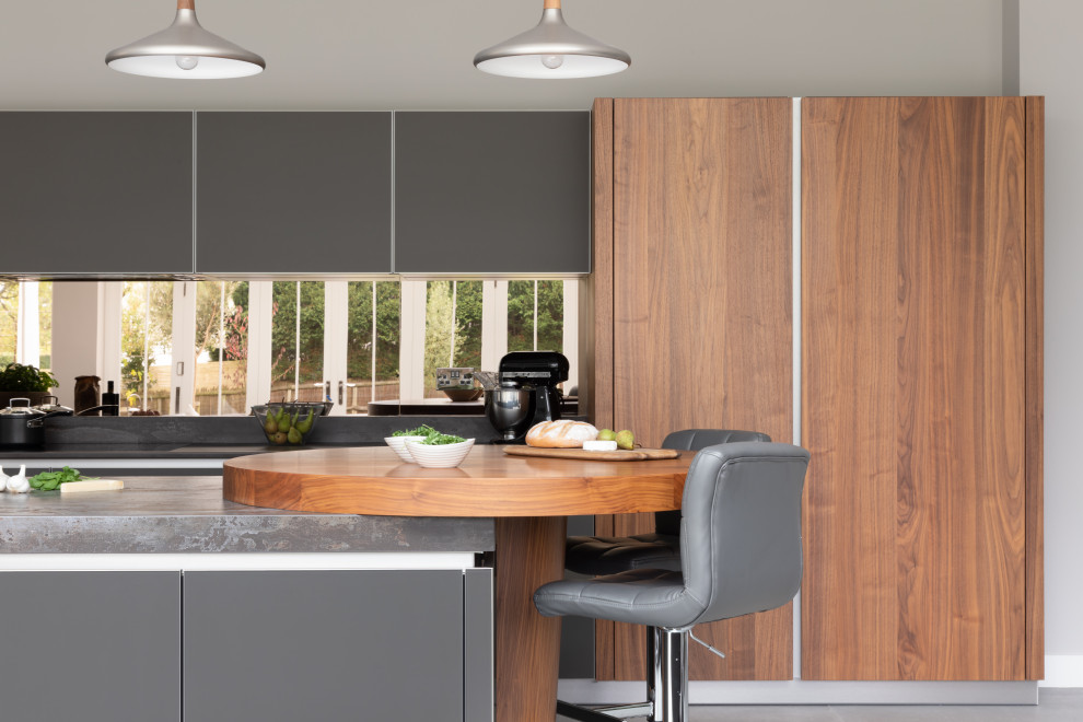 Idéer för ett stort modernt grå kök med öppen planlösning, med en integrerad diskho, luckor med glaspanel, grå skåp, bänkskiva i kvartsit, stänkskydd med metallisk yta, spegel som stänkskydd, svarta vitvaror och en köksö
