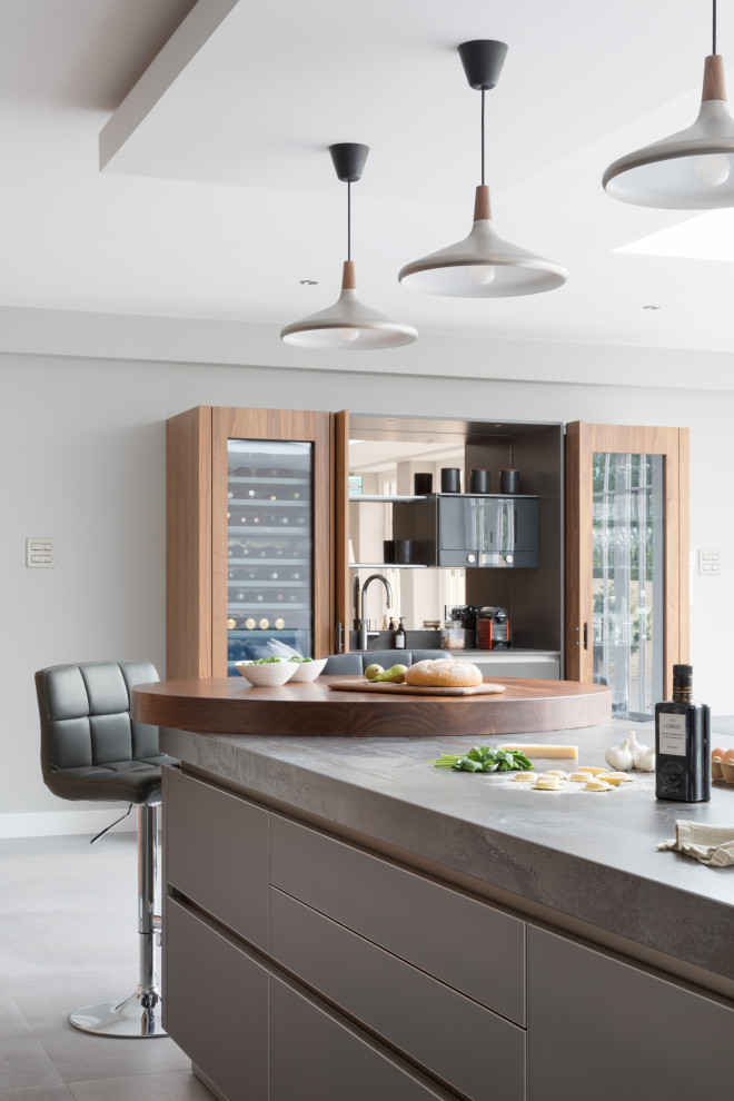 Modern inredning av ett stort grå grått kök med öppen planlösning, med en integrerad diskho, luckor med glaspanel, grå skåp, bänkskiva i kvartsit, stänkskydd med metallisk yta, spegel som stänkskydd, svarta vitvaror och en köksö