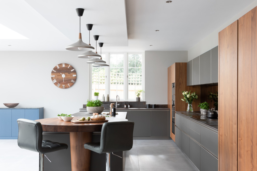 Photo of a large contemporary open plan kitchen in Hampshire with an integrated sink, glass-front cabinets, grey cabinets, quartz worktops, metallic splashback, mirror splashback, black appliances, an island and grey worktops.