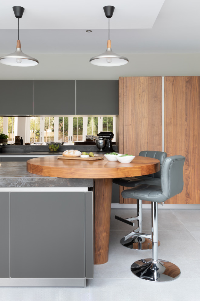 Inspiration for a large contemporary open plan kitchen in Hampshire with an integrated sink, glass-front cabinets, grey cabinets, quartz worktops, metallic splashback, mirror splashback, black appliances, an island and grey worktops.