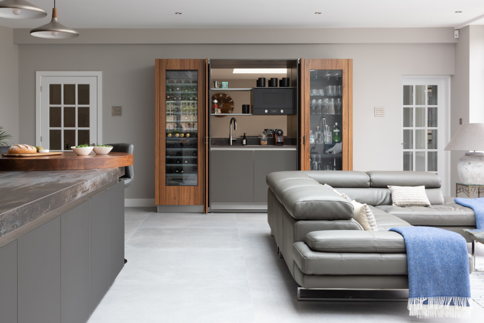 Design ideas for a large contemporary open plan kitchen in Hampshire with an integrated sink, glass-front cabinets, grey cabinets, quartz worktops, metallic splashback, mirror splashback, black appliances, an island and grey worktops.