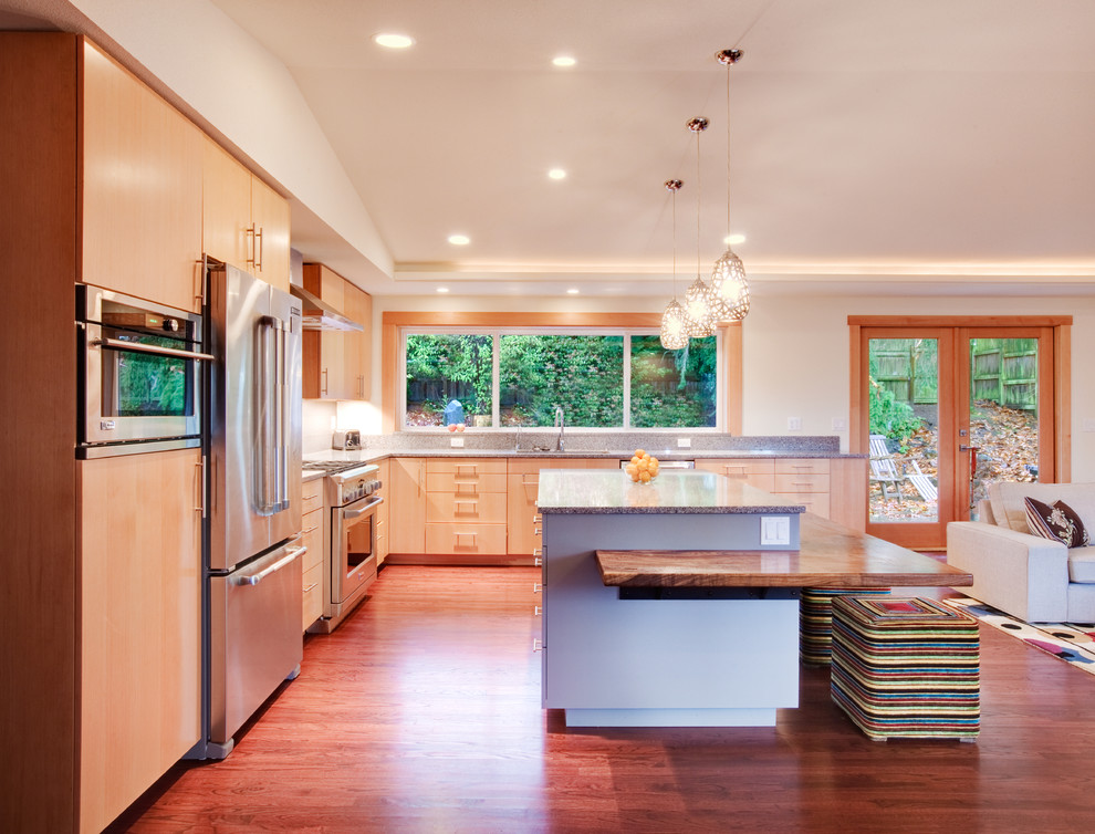 Immagine di una cucina a L minimal con ante lisce, elettrodomestici in acciaio inossidabile e ante in legno chiaro