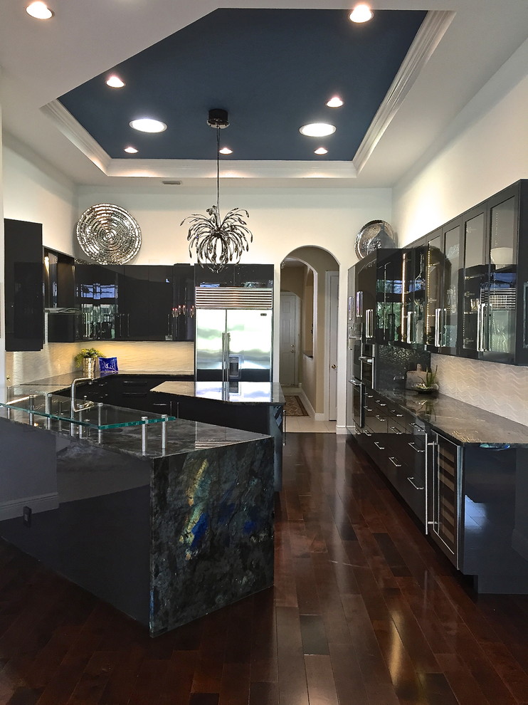 This is an example of a large contemporary u-shaped kitchen/diner in Miami with a submerged sink, glass-front cabinets, black cabinets, white splashback, stainless steel appliances, dark hardwood flooring and an island.