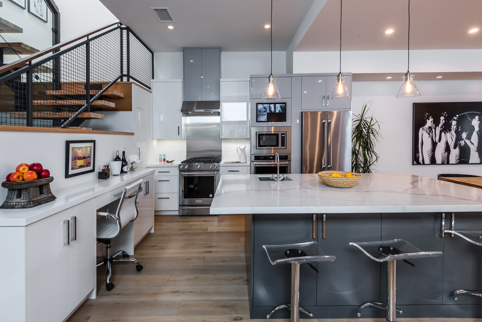 This is an example of a contemporary l-shaped kitchen in Los Angeles with a submerged sink, flat-panel cabinets, white cabinets, stainless steel appliances, medium hardwood flooring, an island and brown floors.