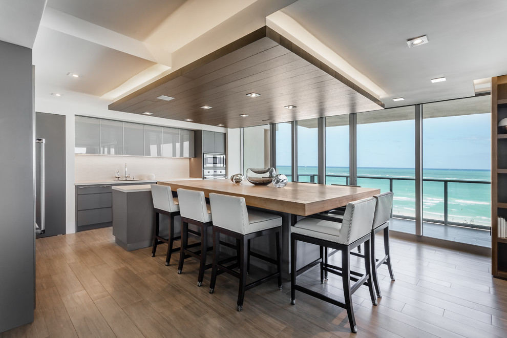 Zweizeilige Moderne Wohnküche mit flächenbündigen Schrankfronten, grauen Schränken, Küchengeräten aus Edelstahl, dunklem Holzboden, Kücheninsel und braunem Boden in Santa Barbara