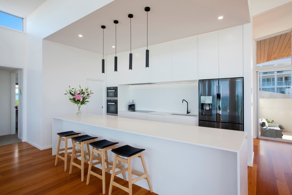 Idéer för ett modernt kök, med en dubbel diskho, släta luckor, vita skåp, vitt stänkskydd, svarta vitvaror, mellanmörkt trägolv, en köksö och orange golv
