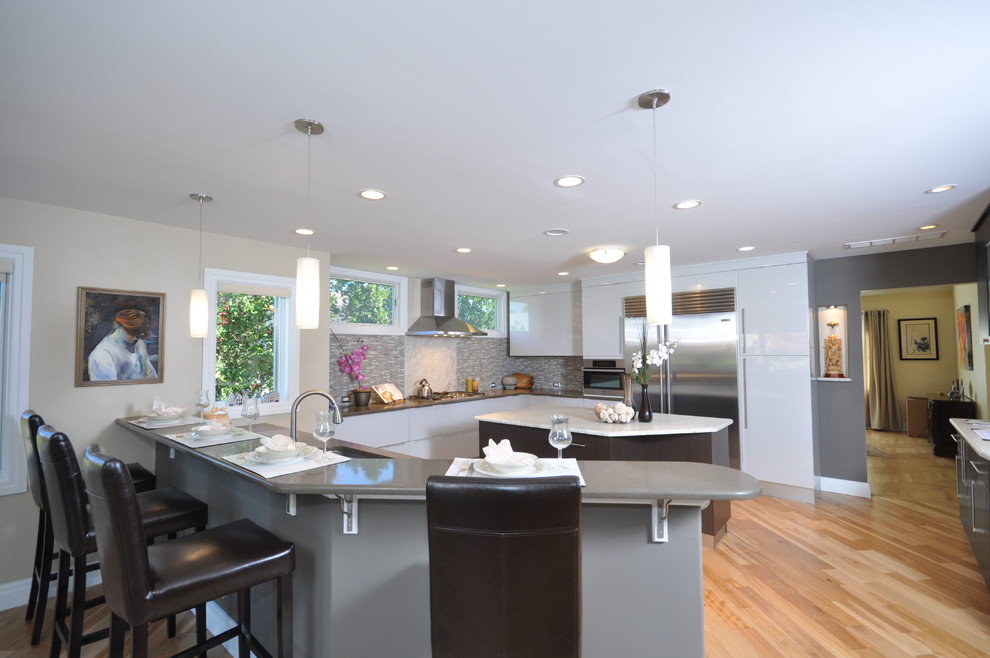 Photo of a large contemporary l-shaped kitchen/diner in Philadelphia with a submerged sink, flat-panel cabinets, white cabinets, granite worktops, grey splashback, mosaic tiled splashback, stainless steel appliances, light hardwood flooring and an island.