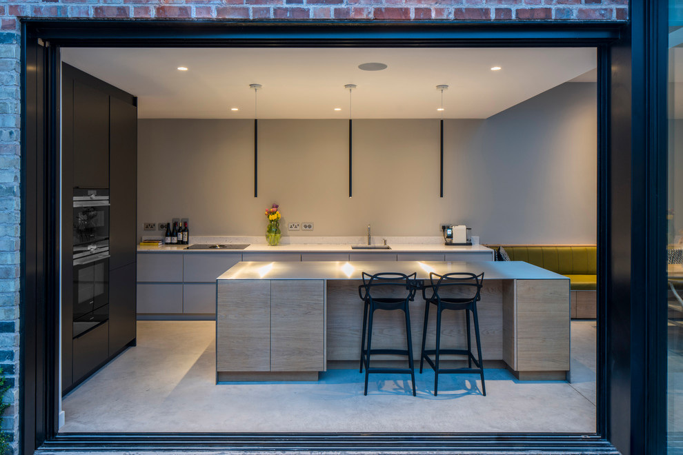 Foto på ett mellanstort funkis kök, med släta luckor, skåp i ljust trä, en köksö, en undermonterad diskho, svarta vitvaror, betonggolv och grått golv
