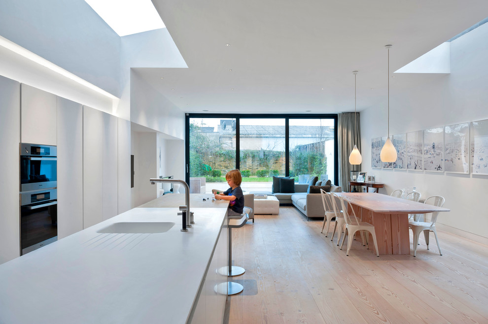 Moderne Küche mit Kücheninsel, weißen Schränken, Küchengeräten aus Edelstahl, integriertem Waschbecken und hellem Holzboden in London